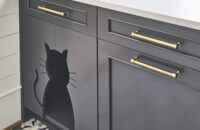 Custom cabinets from Dura Supreme Cabinetry that are hand-crafted and made in America. This gray painted cabinet includes a cat cut out for the cat of the home to access it's hidden food dish.